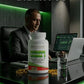 Man in a suit sitting at a desk with a bottle of Nordic Naturals Omega-3 supplement, surrounded by technology.